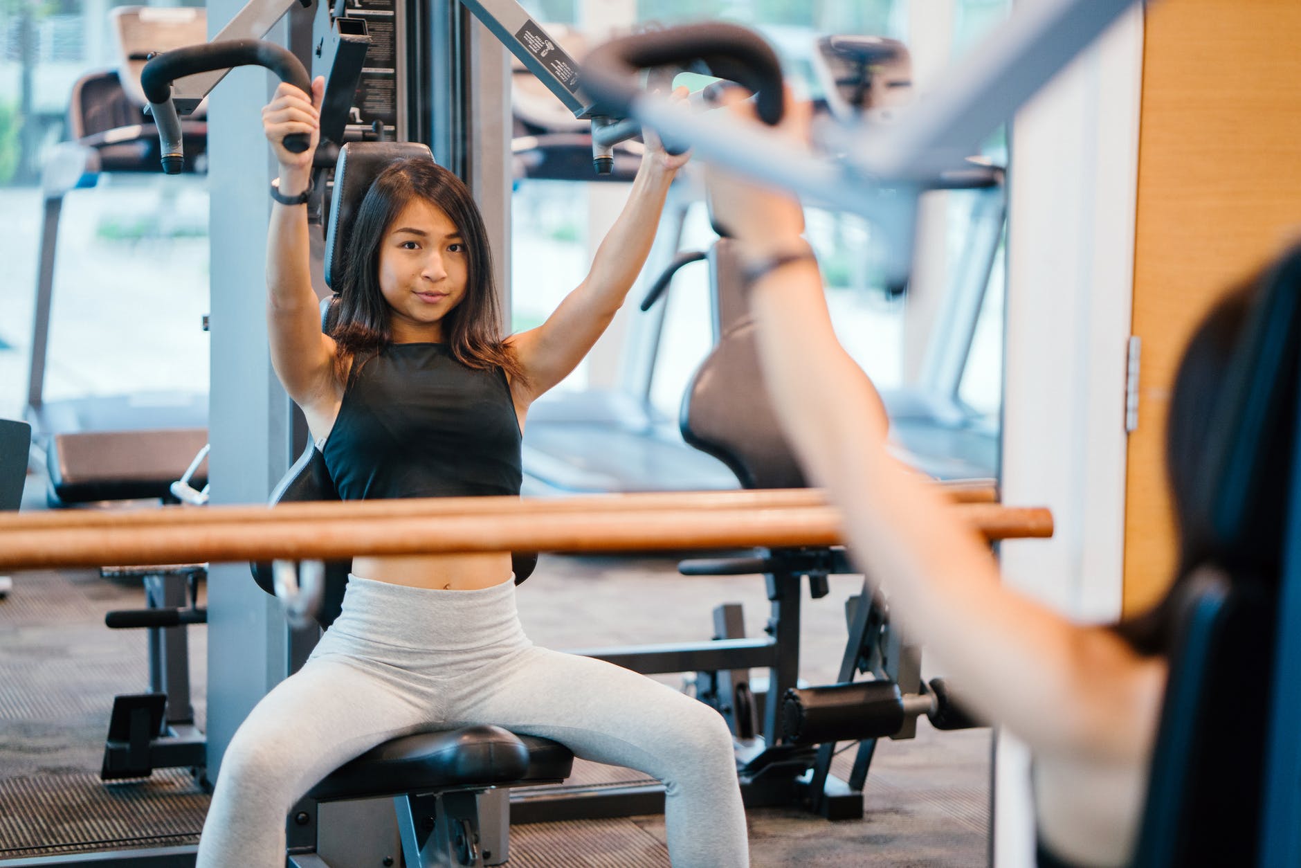 woman in black sleeveless crop top and white leggings using a butterfly machine in front of a mirror